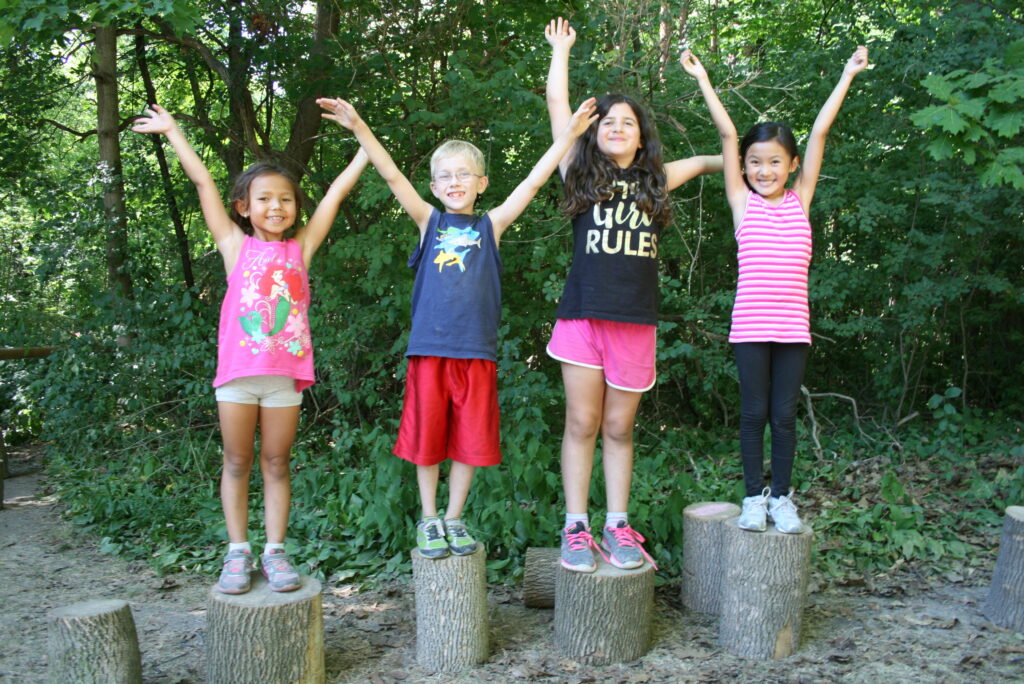 Kids in Nature standing on logs with arms up in air smiling